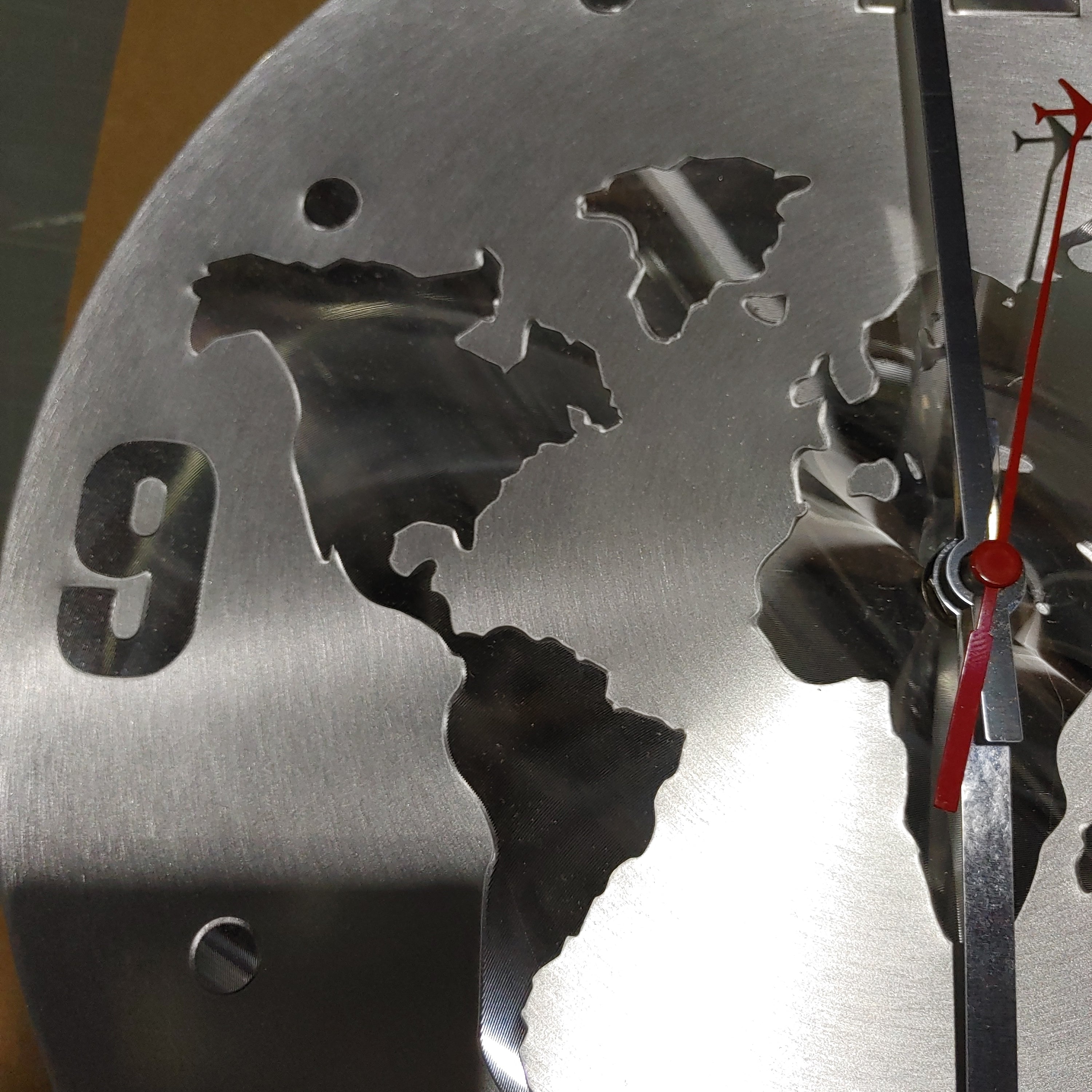 Wall clock metal world with continents and red airplane on hand